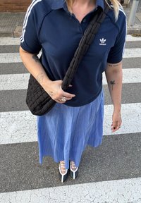 Polo da Adidas em azul-marinho com riscas brancas, saia plissada azul-claro, mala de ombro acolchoada preta e sapatos de atacadores bicolores.