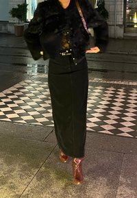 Μαύρο ψεύτικο γούνινο cropped τζάκετ πάνω από ένα διάτρητο τοπ, συνδυασμένο με μια μακριά μαύρη φούστα και καφέ μποτάκια έως τον αστράγαλο. Το σκηνικό διαθέτει μια καρό πλακόστρωτη επιφάνεια.