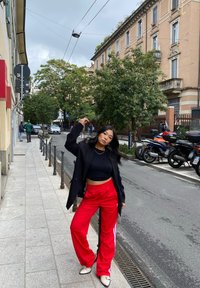 Svart oversized blazer, åtsittande svart crop top och röda sportbyxor med vita ränder. Gågata med byggnader och grönska i bakgrunden.