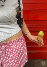 Grå t-shirt och röd-vit rutiga shorts, håller en strut med grön glass; strukturerad vägg i bakgrunden.