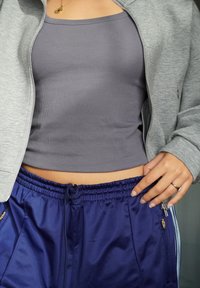 Chaqueta gris con cremallera, top gris acanalado y pantalones cortos deportivos azul marino con cordón y bolsillos laterales, con una textura brillante.