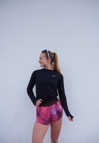 Svart langermet treningsskjorte med tommelhull, kombinert med livlige rosa og lilla mønstrede shorts med svart midjebånd.