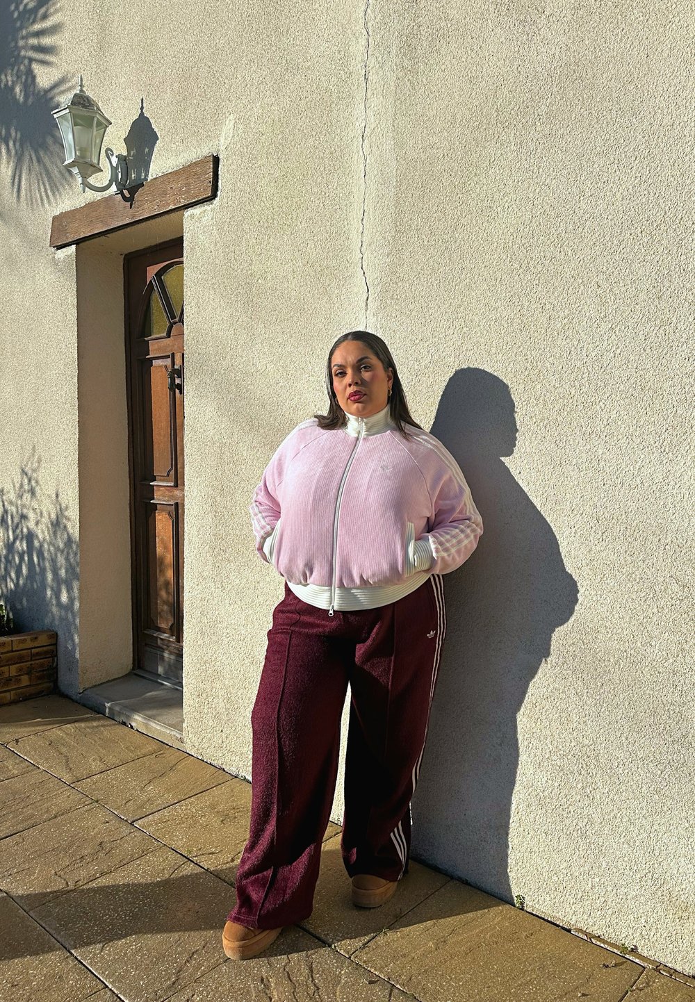 Veste zippée en velours côtelé rose clair avec des accents blancs et des poignets assortis, associée à un pantalon large bordeaux avec des rayures blanches.