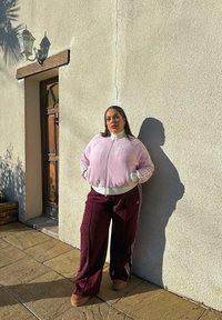 Veste zippée en velours côtelé rose clair avec des accents blancs et des poignets assortis, associée à un pantalon large bordeaux avec des rayures blanches.