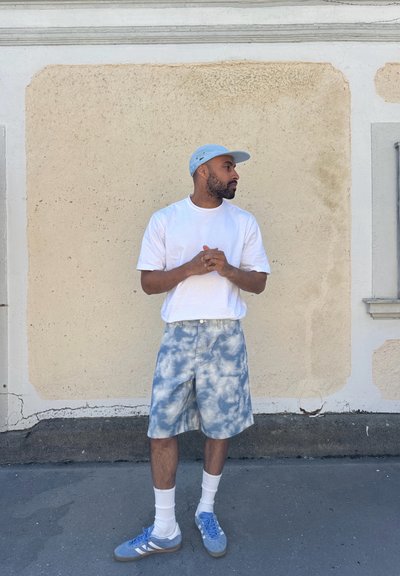 Camiseta blanca, pantalones cortos azul claro con patrón de nubes, calcetines blancos y zapatillas azul claro. Una gorra azul claro completa el atuendo.