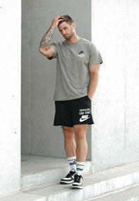 T-shirt cinza da Nike com texto preto, calções pretos com a inscrição branca "APENAS PARA USO OFICIAL" e sapatilhas pretas com detalhes brancos.