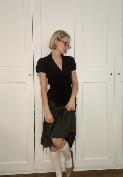 Blusa negra con mangas cortas, combinada con una falda oscura y fluida. Medias blancas hasta la rodilla y zapatos grises completan el conjunto.