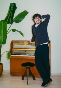 Eiket oppreist piano med synlige mekaniske deler, ledsaget av en svart krakk. En stor grønn plante står i bakgrunnen mot en lys vegg.