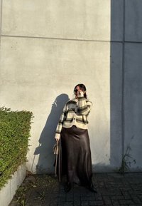 Prúžkovaný kardigán v krémovej, olivovej a hnedej vlne cez hnedú koženú maxi sukňu. Čierne topánky a šedá kabelka. Tieň na stene.