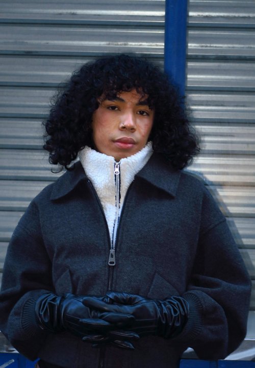 Veste en fausse fourrure dans des tons de marron, coupe oversized, portée avec un jean noir et des bottes en cuir marron. Tenant un sac à main en cuir noir.