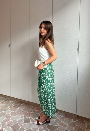 Falda midi verde con flores blancas, combinada con una camiseta sin mangas blanca y zapatos de tacón bloque marrones con puntas blancas. Bolso de mano blanco.