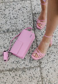 Ροζ ψηλοτάκουνα πέδιλα με σταυρωτές λωρίδες και τετράγωνη μύτη, σε συνδυασμό με μια ροζ τσάντα χιαστί που διαθέτει κούμπωμα και λουρί ώμου.