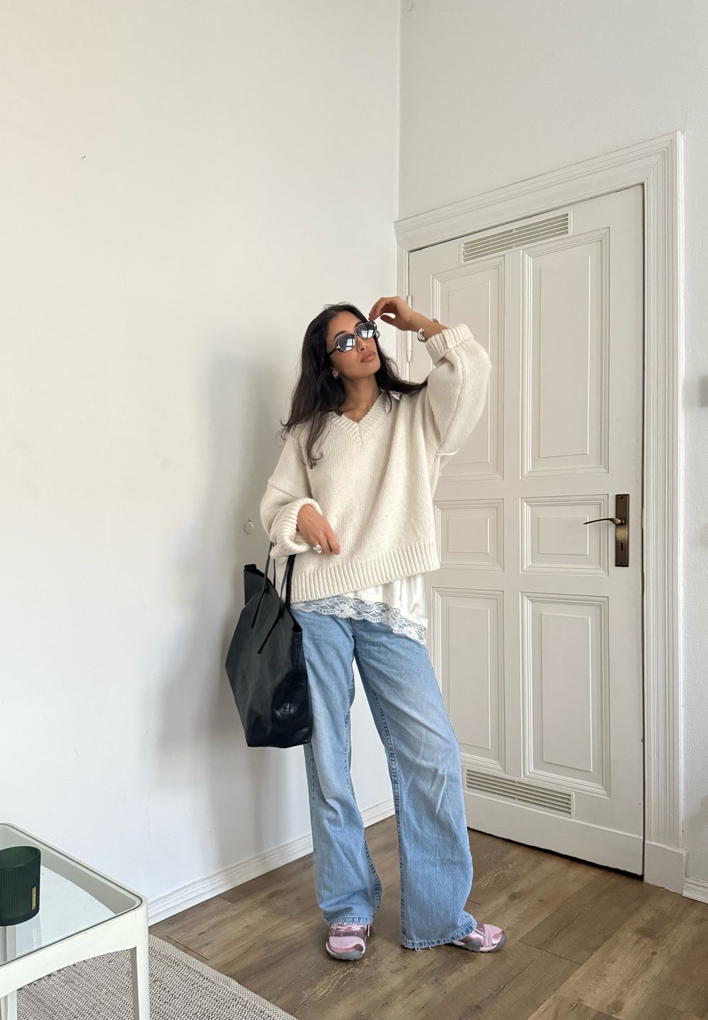 Pull en maille crème surdimensionné avec détail en dentelle légère, associé à un jean bleu délavé ample. Sac fourre-tout noir, sandales roses, cadre intérieur.