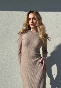 Beige Langarmkleid aus geripptem Strick mit runder Halslinie, taillierter Silhouette und weichem Textur, vor einem neutralen Hintergrund mit sanften Schatten.