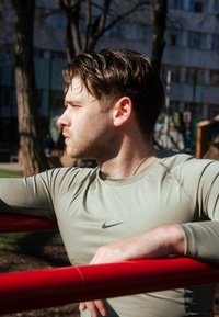 Langærmet, olivengrøn træningsshirt med en tætsiddende pasform og Nike-logo på brystet, parret med en rød støttebånd.