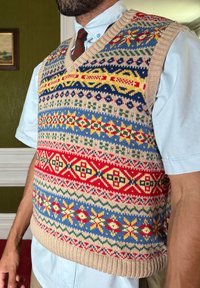 Πλεχτό γιλέκο με βαθύ λαιμόκοψη, με πολύχρωμα γεωμετρικά σχέδια σε μπεζ φόντο. Τα υλικά περιλαμβάνουν μαλλί και βαμβάκι.