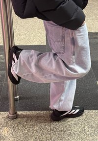 Črne superge z belimi črtami, kombinirane s svetlo moderimi širokimi kavbojkami. Superge imajo gladko teksturo in zaobljene podplate.