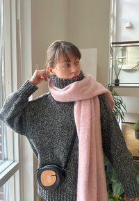 Πουλόβερ χοντρής γκρίζας πλέξης με ψηλό γιακά, σε συνδυασμό με ένα μαλακό ροζ κασκόλ. Μια μικρή μαύρη στρογγυλή τσάντα χιαστί ολοκληρώνει το σύνολο.