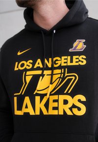 Zwarte hoodie met in vette gele tekst "Los Angeles Lakers". Inclusief een Lakers-logo en zwarte drawstrings met gele punten. Zachte stof textuur.