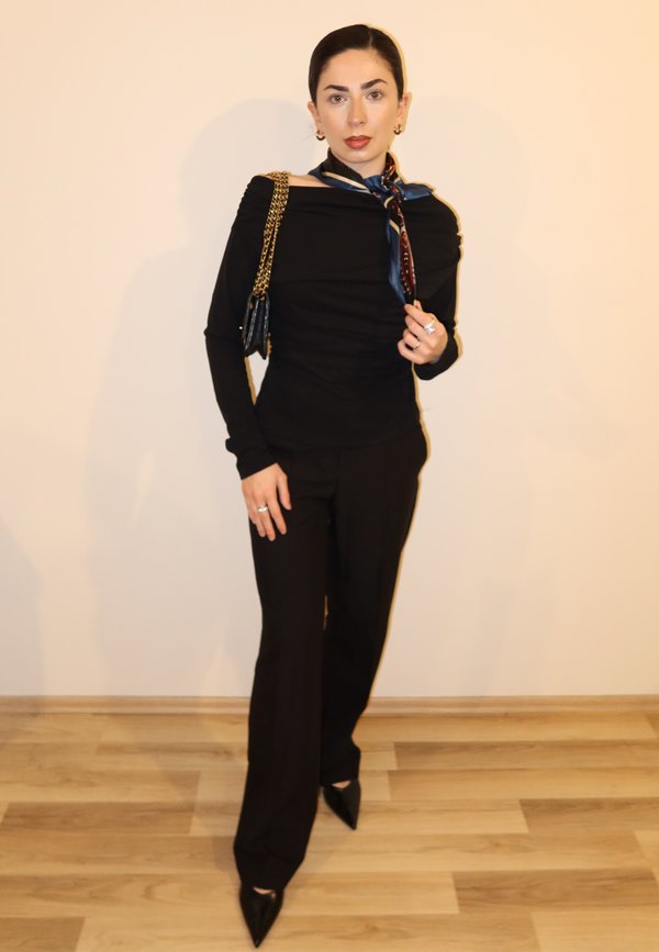 Žena v černém oblečení s dlouhými rukávy a kalhotami, s šátkem a nesoucí černou kabelku se zlatým řetízkem.