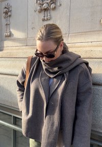 Grå ullkappa med en stor, draperad krage, lager på lager över en ljus topp. Tillbehören inkluderar mörka solglasögon och en brun axelväska.