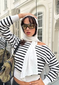 Gestreepte trui in wit en zwart, cropped stijl, gecombineerd met een lichte sjaal. Geaccessoireerd met oversized zonnebril en een gestructureerde handtas.