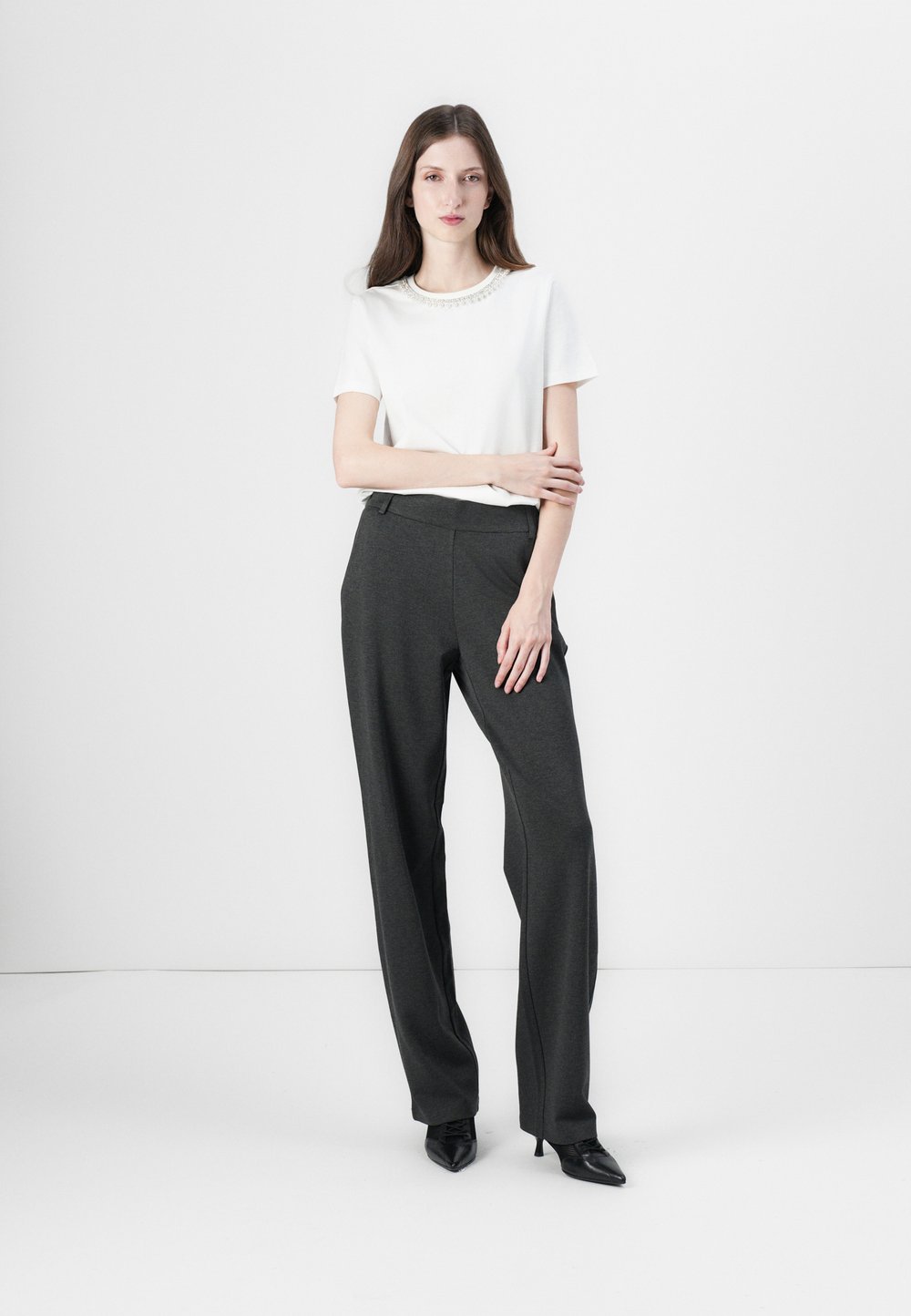 Balta trumpomis rankovėmis marškinėliai su puošniu apykakle, derinama su aukštu liemeniu tamsiai pilkais kelniais. Modelis vilki juodas smailianosias aukštakulnes.