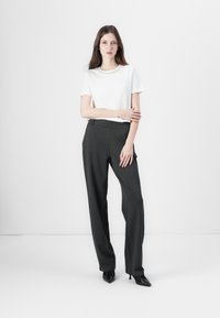 Balta trumpomis rankovėmis marškinėliai su puošniu apykakle, derinama su aukštu liemeniu tamsiai pilkais kelniais. Modelis vilki juodas smailianosias aukštakulnes.