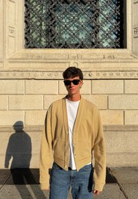 Črtasti kardigan rumene in bele barve, lahkega materiala, krajši kroj, z zapenjanjem na gumbe, kombiniran s preprosto belo majico in modrimi kavbojkami.