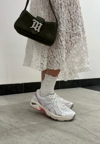 Biely čipkovaný šaty, po kolená, vrstvená textúra; šedé a ružové športové topánky s dizajnom z pletiva; olivovozelená kabelka s striebornými kovovými prvkami; rebrované biele ponožky.