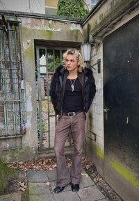 Μαύρο γελέκο από faux γούνινη ύφανση με δερμάτινη εσωτερική επένδυση, μαύρο τοπ με αθλητική εφαρμογή, καφέ φαρδιά παντελόνια και μαύρα παπούτσια; στυλιζαρισμένο με διαδοχικά κολιέ.