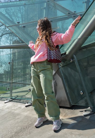 Conjunto casual que incluye una sudadera rosa, pantalones cargo verdes y zapatillas ligeras rosas. Accesorios con un bolso burdeos con tachuelas plateadas.
