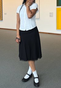 Črna krila do kolen z resicami, v kombinaciji z belim kratkolesnim srajcem. Črne Mary Jane čevlje in bele gležnjarje dopolnjujejo videz.