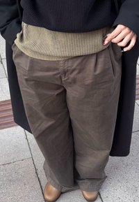 Laza szabású, khaki nadrágok texturált, bordázott bézs felsővel. Az öltözék magas derékvonallal és puha anyaggal rendelkezik, kiegészítve barna lábbelivel.