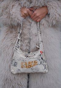 Fehér szövet válltáska fekete vázlatokkal és narancssárga "DESIGNED" felirattal. Fonott pántokkal és textúrált, puha háttérrel rendelkezik.