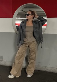 Μαύρο δερμάτινο μπουφάν, μπεζ τοπ αμάνικο και χακί παντελόνι φαρδύ. Γυαλιά ηλίου, υφές και κυκλική πίσω όψη καθρέπτη.