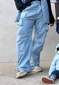 Light blue cargo trousers with a relaxed fit, featuring multiple pockets, an elasticated waistband, and a smooth, slightly shiny texture.