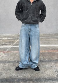 Šedá mikina na zip s předními kapsami, kombinovaná s volnými světle modrými džínami. Černé tenisky doplňují ležérní vzhled.