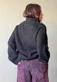 Svart, fluffig, överdimensionerad tröja med hög krage; bärs med djupt lila, löst sittande byxor med bakfickor. Slät struktur och avslappnad passform.