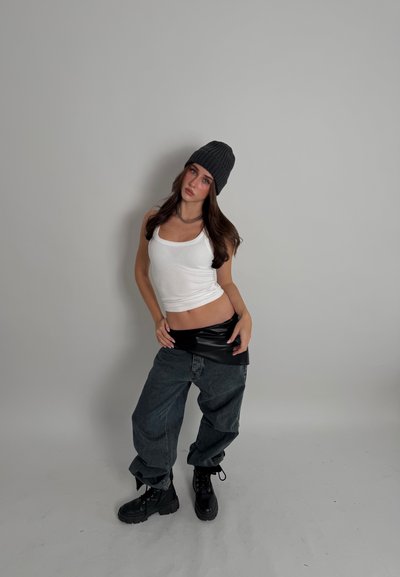 Camiseta sin mangas blanca, envoltura de cuero negro, vaqueros oscuros holgados y botas negras con cordones; combinado con un gorro de punto gris y un collar de cadena plateada.