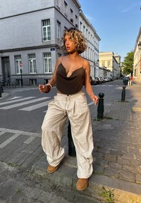 Bruine coltrui met dunne banden, beige baggy broek met cord, en tan enkellaarzen, tegen een stadstraat achtergrond.