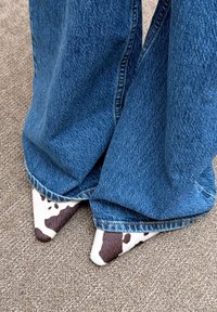 Chaussures à bout pointu avec texture imprimé vache; associées à un jean en denim bleu à jambes larges, légèrement trainant sur un tapis beige.