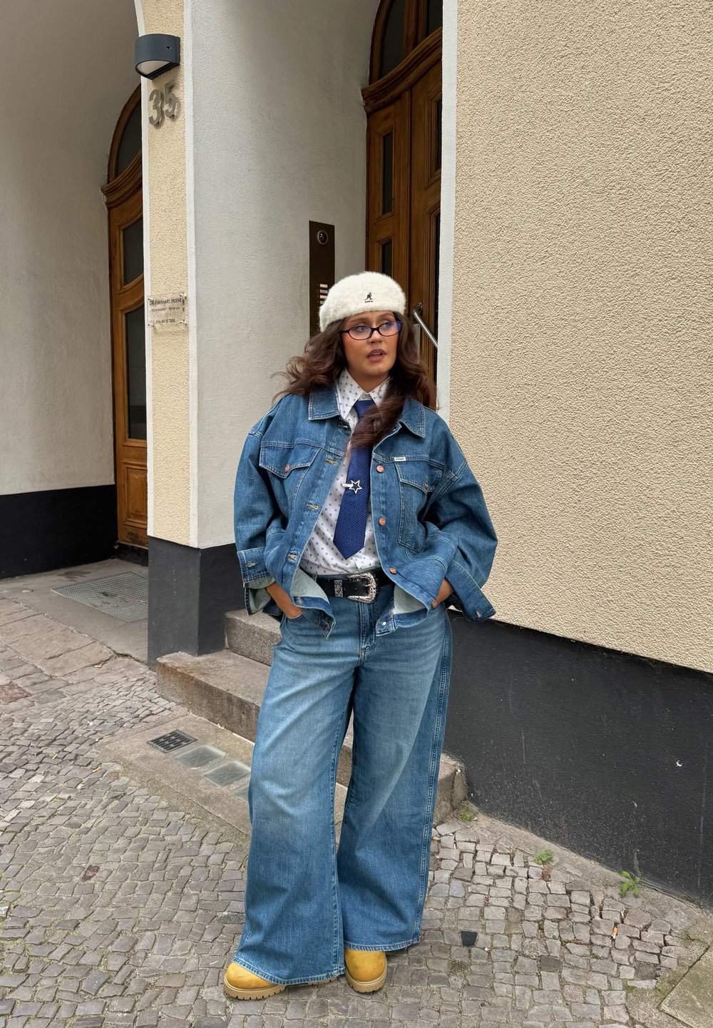 Sinine teksajope, oversized sobivate lõikega, helesinised laiad teksapüksid, valge mustriga särk, sinine lips ja beeži platvormkingad, koos kreemja kudumisega mütsiga.