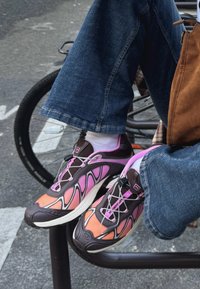 Sportske tenisice s višebojnim dizajnom u kojem dominiraju narančasta, ružičasta i smeđa. Gornji dio ima teksturiranu mrežu i potporne elemente blizu vezica.