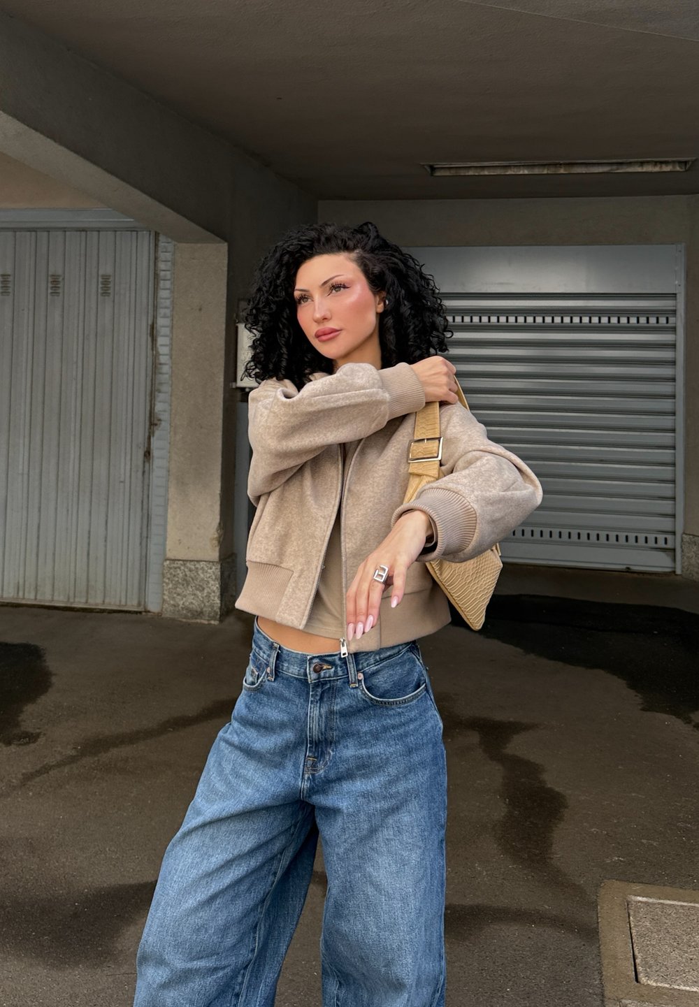 Beige kort jakke med myk tekstur, båret over en matchende topp og sammen med løse blå denimjeans. Flettet beige veske og sølvring.