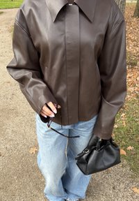 Brun läderjacka med krage och mittsöm, kombinerad med blå vida jeans. Håller i solglasögon och en svart handväska.