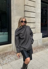 Maglione oversize in misto lana grigio con collo alto, caratterizzato da maniche lunghe e spacchi laterali, abbinato a una gonna di pelle e stivali fino al ginocchio.