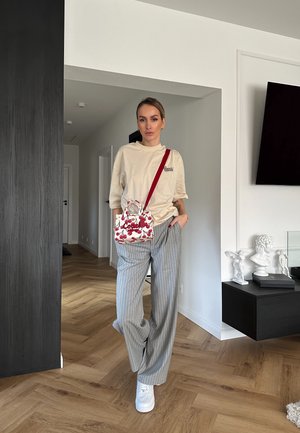 Camiseta oversized beige, pantalones anchos de rayas verticales grises, zapatillas blancas y un pequeño bolso blanco con estampado de cerezas rojas y asas.