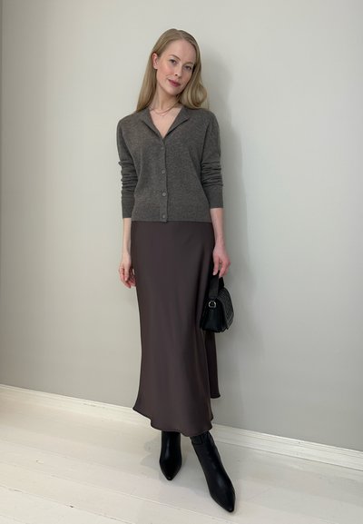 Cárdigan gris de botones, vestido midi marrón ajustado y elegante, botas negras de tacón puntiagudo y un pequeño bolso negro texturizado. Diseño simple y ceñido.