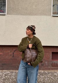 Pull en maille vert à manches larges, jean bleu à jambe large, sac à main en cuir marron et foulard à motif camouflage. Créoles en or.